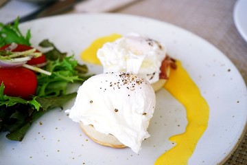 Two eggs benedicts, breakfast menu, consist of eggs, english muffin, canadian bacon and Hollandaise sauce served with salad placed on white dish.