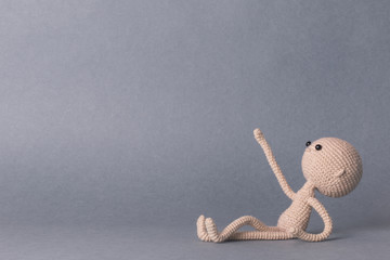 A toy man on a gray background with space for text. Knitted toy amigurumi. Presentation. Motivational phrase. Cute model. Puppet. Sweet doll. Hand up. Relax.