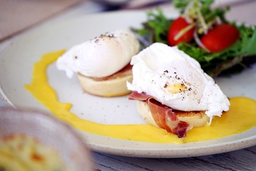 breakfast is egg benedict,consist of eggs, english muffin, canadian bacon and Hollandaise sauce served with salad placed on white dish.