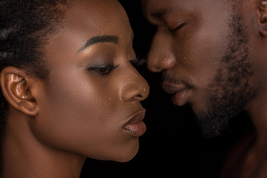 side view of young african american couple with water drops on faces posing isolated on black
