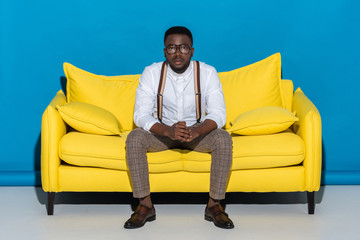 young african american man in eyeglasses sitting on sofa and looking at camera