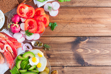 Ingredients for the preparation of a traditional Danish open sandwich called Smorrebrod on rye bread with vegetables, red fish, shrimps, eggs, herring and greens. Top view, horizontal, copy space.