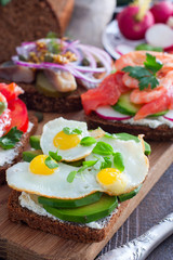 An open sandwich with avocado, quail eggs and fresh basil greens on rye bread with curd cheese, selective focus