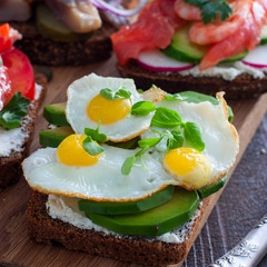 An open sandwich with avocado, quail eggs and fresh basil greens on rye bread with curd cheese, selective focus