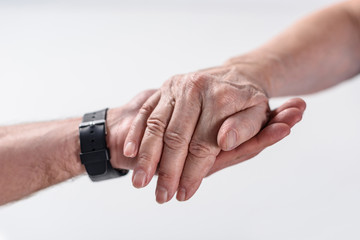 cropped shot of senior man and rehabilitation therapist holding hands isolated on grey