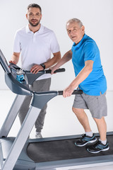 Fototapeta na wymiar rehabilitation therapist and senior man on treadmill isolated on grey