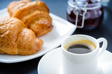 White cup of coffee and two croissants with jam on the table