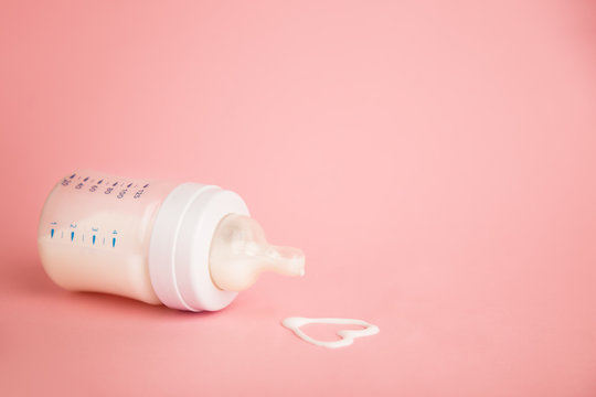 Baby Milk Bottle On A Pink Background With Neagtive Space. Spill