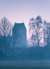 Historical church and winter trees in morning mist. Dutch rural village, Geesteren, Gelderland, Achterhoek.