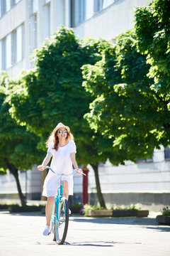 Vertical full length of ajoyful young woman in a dress smiling enjoying riding a bike in the city center on a sunny summer day copyspace outdoors nature activity summertime cycling.