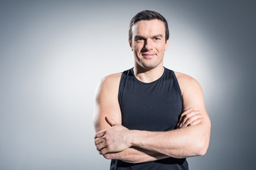 Fototapeta premium Sportsman standing with folded arms on grey background