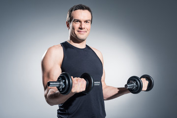 Plakat Smiling man lifting dumbbells on grey background