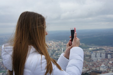 Girl in a white jacket with long hair takes a photo on the phone. Overcast