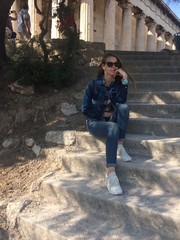 Smiling Caucasian girl in sunglasses. A girl with long hair in a denim suit and white sneakers the girl sits on the steps near the ancient temple with columns. Summertime