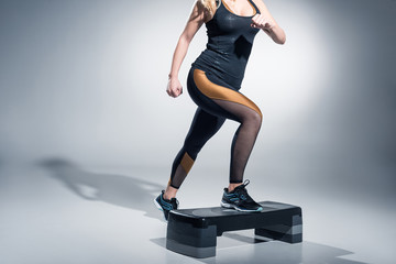 Young woman exercising on step platform on grey background