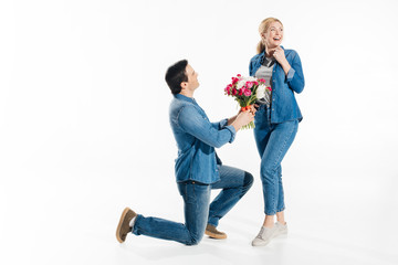 Man standing on one knee and giving happy woman a bouquet of flowers isolated on white