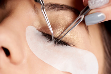 Naklejka premium Brunette woman is getting eyelash extensions in a salon. Close-up
