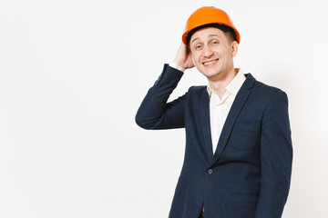 Young handsome overjoyed businessman in dark suit, protective construction orange helmet keeping hand on head isolated on white background. Male worker for advertisement. Business, working concept.