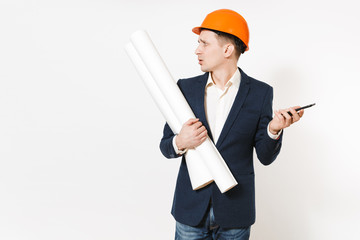 Young dissatisfied businessman in dark suit, protective hardhat holding blueprints plans and mobile phone and looking aside on copy space isolated on white background. Male worker for advertisement.