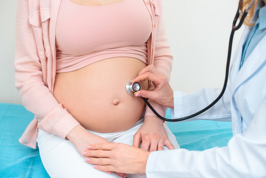 cropped shot of obstetrician gynecologist listening heartbeat of child fetus of pregnant woman with stethoscope