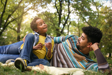 Fototapeta premium African American father lying in meadow with daughter and having conversation.