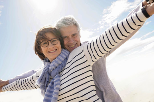 Portrait of senior couple at the beach stretching arms out