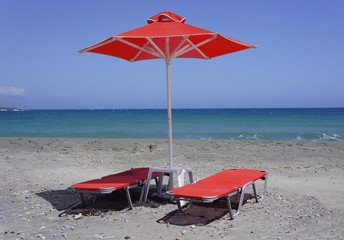 Red sun loungers and a red parasol on the sandy beach, natural beach