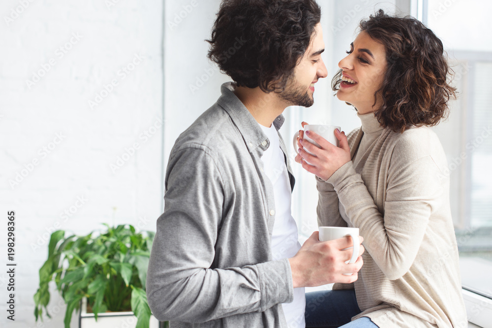 Wall mural young couple laughing and holding cups of tea at home