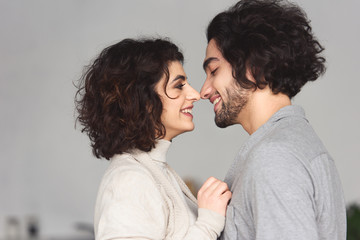 side view of smiling young couple touching with noses at home