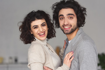 smiling young couple hugging and looking at camera at home