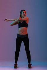 Fototapeta na wymiar Full length portrait of sportswoman in fitness clothing looking aside while stretching her arms, isolated over colorful background