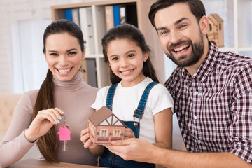 Young family is happy to buy new house, holding keys from house and miniature house.