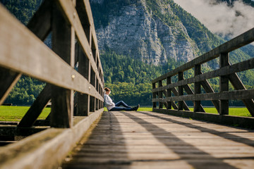 girl is sitting on a wooden bridge. Young tourist woman sits on the bridge and enjoy the relaxation and freedom. Beautiful view of the mountain nature
