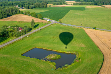 Cień balonu lecącego nad polami ze stawem, w dole widać drogi i pola uprawne. - obrazy, fototapety, plakaty