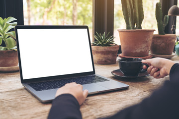 Mockup image of woman using and typing on laptop with blank white desktop screen while drinking coffee in cafe
