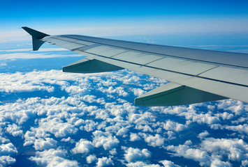 Obraz premium Airplane wing out of window, blue sky and clouds