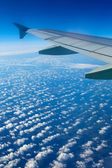 Obraz premium Airplane wing out of window, blue sky and clouds