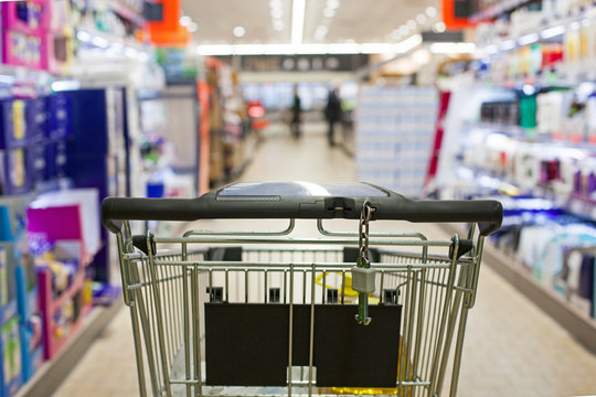 Shopping cart full of grocery on blurred supermarket aisle.
