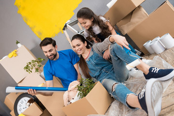 Happy father and wife and daughter sort things out from cardboard boxes in house they moved.
