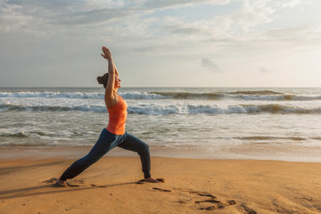 Fototapeta na wymiar Woman doing yoga asana Virabhadrasana 1 Warrior Pose on beach on