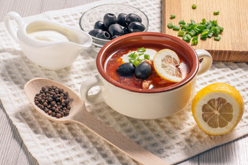 Soup saltwort with meat, potatoes, tomatoes, lemon, black olives and sour cream in ceramic soup bowl