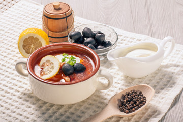 Soup saltwort with meat, potatoes, tomatoes, lemon, black olives and sour cream in ceramic soup bowl