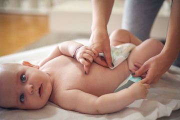 Mother changing diapers her  little baby boy at home. Close up.