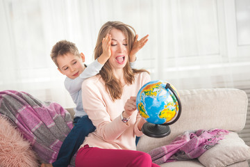 Young mom helping her son to do homework. Family choosing where to travel on vacation. Mother and her child holding a globe