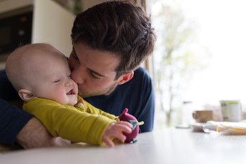 Young father kissing with baby boy at breakfast table