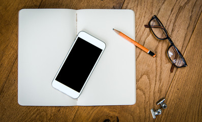  top view of open book and glasses with smartphone and pencil on wooden desk