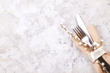 Easter table setting composition: fork, knife silverware wildflowers, pussy willow on plate w/ napkin, white stucco plaster texture background. Close up, top view, copy space