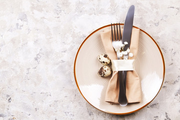 Easter table setting composition: quail eggs, candle, wilflowers, pussy willow on plate w/ napkin, white stucco plaster texture background. Close up, top view, copy space, greeting, template.