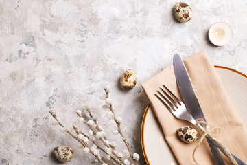 Easter table setting composition: quail eggs, candle, wilflowers, pussy willow on plate w/ napkin, white stucco plaster texture background. Close up, top view, copy space, greeting, template.