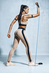 Fototapeta na wymiar Woman exercising with resistance band. Photo of sporty woman in sportswear workout on grey background. Strength and motivation